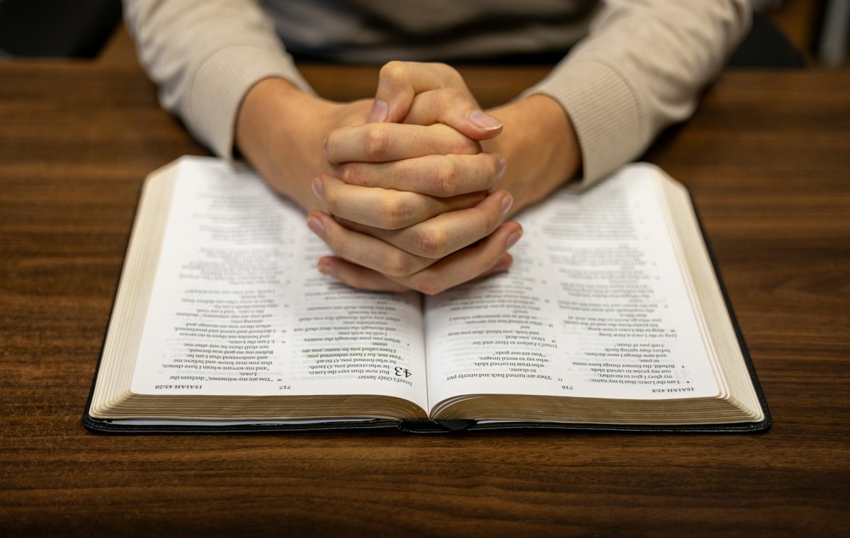Hands folded in prayer over an open Bible