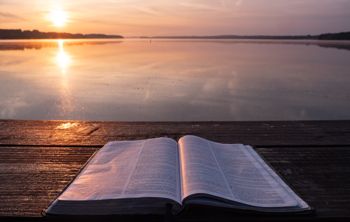 An open Bible resting on a jetty at sunset